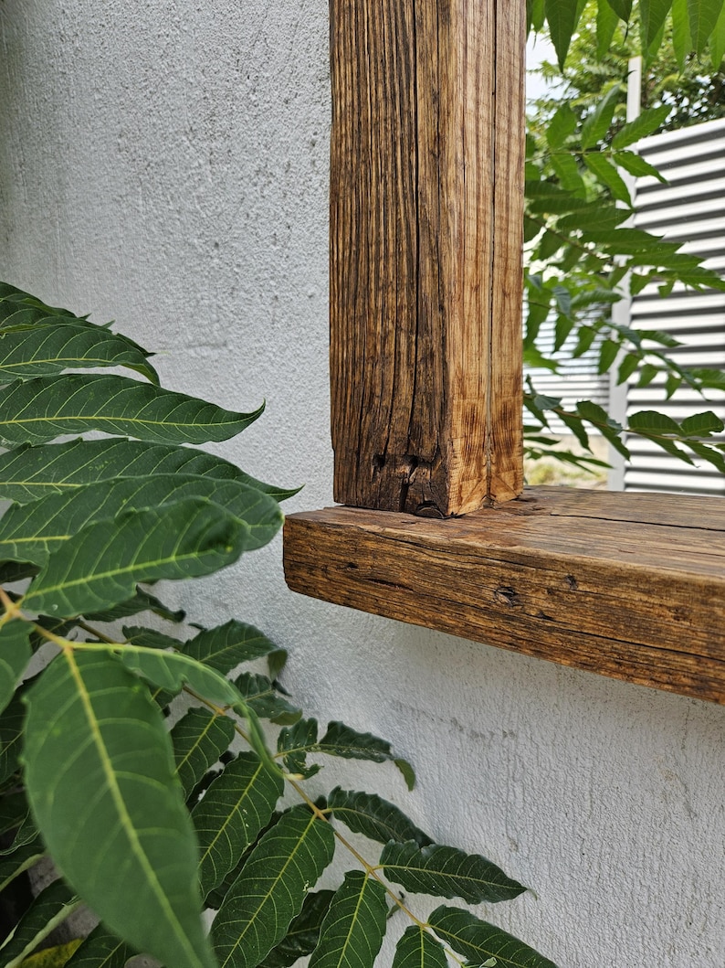 May include: Close-up of a wooden frame with a weathered, brown finish. The frame is mounted to a white wall and has a thick, horizontal top piece.