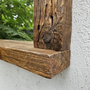 May include: Close-up of a rustic wooden mirror frame with a natural wood finish. The frame is made of thick, reclaimed wood planks with knots and grain patterns. The frame is mounted on a white wall.
