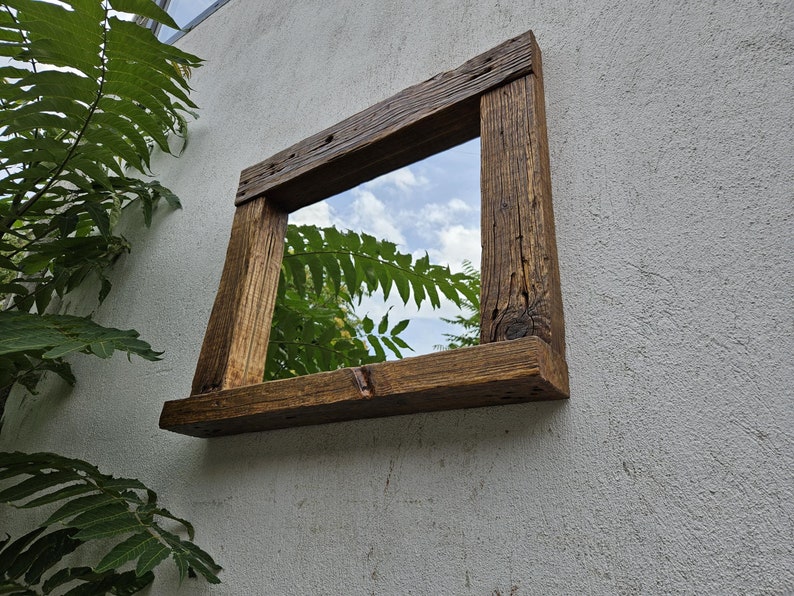 May include: A rustic wooden mirror with a shelf, featuring a natural wood finish and a rectangular shape. The mirror reflects a view of a tree and sky.