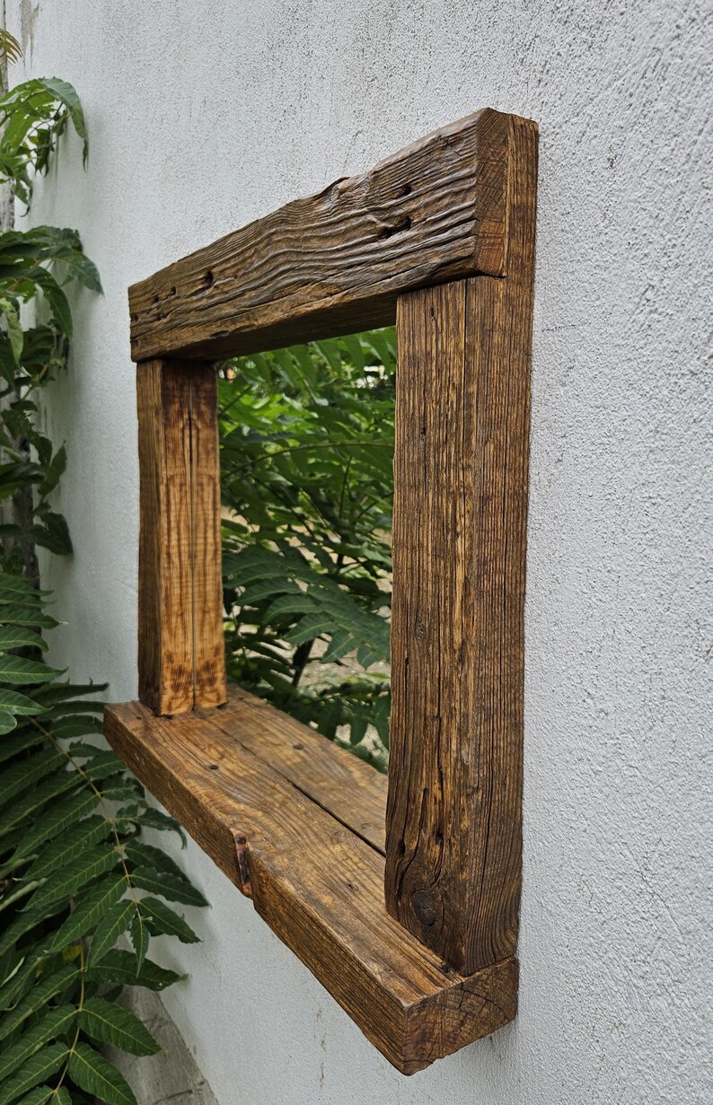 May include: A rustic wooden mirror with a shelf. The mirror is framed in reclaimed wood with a natural brown finish. The shelf is made of the same wood and is attached to the bottom of the frame.