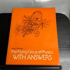 May include: A bright orange book titled The Flying Circus of Physics WITH ANSWERS by Jearl Walker. The cover features a detailed black line drawing of a complex, whimsical flying machine with wheels, propellers, and a large spherical structure.