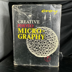 May include: A vintage book titled "Creative Photo Micrography" with a black cover and yellow and red text. The cover features a detailed illustration of a microscopic structure. The book's title is prominently displayed.