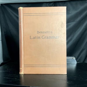May include: A hardcover book titled "Bennett's Latin Grammar" with a brown cover and spine. The title is printed in dark text. The book has a simple, classic design, suggesting it is a textbook or reference book.