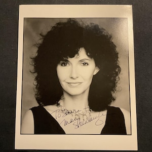 May include: Black and white photograph of a woman with dark, curly hair. She is wearing a black top and a necklace. The photograph is signed "To Steven, Mary Steenburgen".