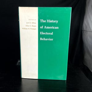 May include: A hardcover book titled "The History of American Electoral Behavior." The book has a green cover with white text and a white spine. The book's editors are listed on the spine. The book is on a black surface.