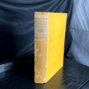 May include: A vintage book titled "The House of Souls" by Arthur Machen. The book has a yellow cover and a tan spine with faded text. The book is standing upright on a dark surface.