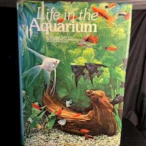 May include: A book titled "Life in the Aquarium" with a colorful illustration of various fish species, aquatic plants, and a piece of driftwood. The cover also includes the text "A Colourful Guide to Freshwater and Marine Animals and Aquatic Plants."