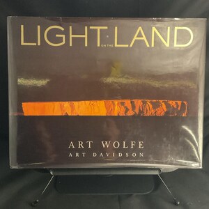 May include: A book titled "LIGHT LAND" with gold lettering on a dark brown background. The cover features an orange and brown landscape image. The author's names, Art Wolfe and Art Davidson, are printed below the image.