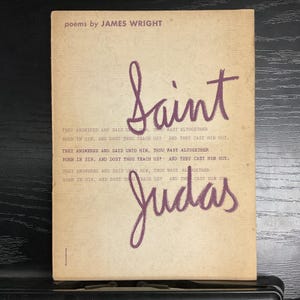 May include: Vintage book cover with the title "Saint Judas" in purple script. The cover is a light tan color with text from the poem printed in a darker font. The author's name, James Wright, is printed at the top.