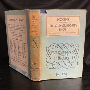 May include: A vintage copy of "The Old Curiosity Shop" by Charles Dickens, part of the Everyman's Library series. The book features a light blue cover with gold lettering and a decorative logo. The spine is a faded green with the title and author's name.