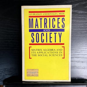 May include: A yellow book titled "Matrices and Society" with text in blue and red. The book's subtitle reads "Matrix Algebra and Its Applications in the Social Sciences." The book has a price tag in the bottom left corner.