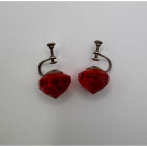 May include: A pair of vintage screw-back earrings. Each earring features a faceted, red, gem-like pendant. The pendants are diamond-shaped and attached to silver-toned metal screw-back findings. The earrings are displayed against a white background.