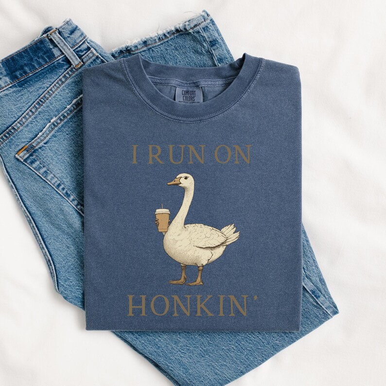 May include: A navy blue t-shirt with the text "I run on honkin'" in brown lettering. A cartoon goose holding a cup of coffee is pictured below the text.