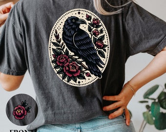 Puede incluir: Una camiseta negra con una ilustración de estilo vintage de un cuervo posado en una rama con rosas rojas. El cuervo está rodeado por un círculo de pequeños puntos.
