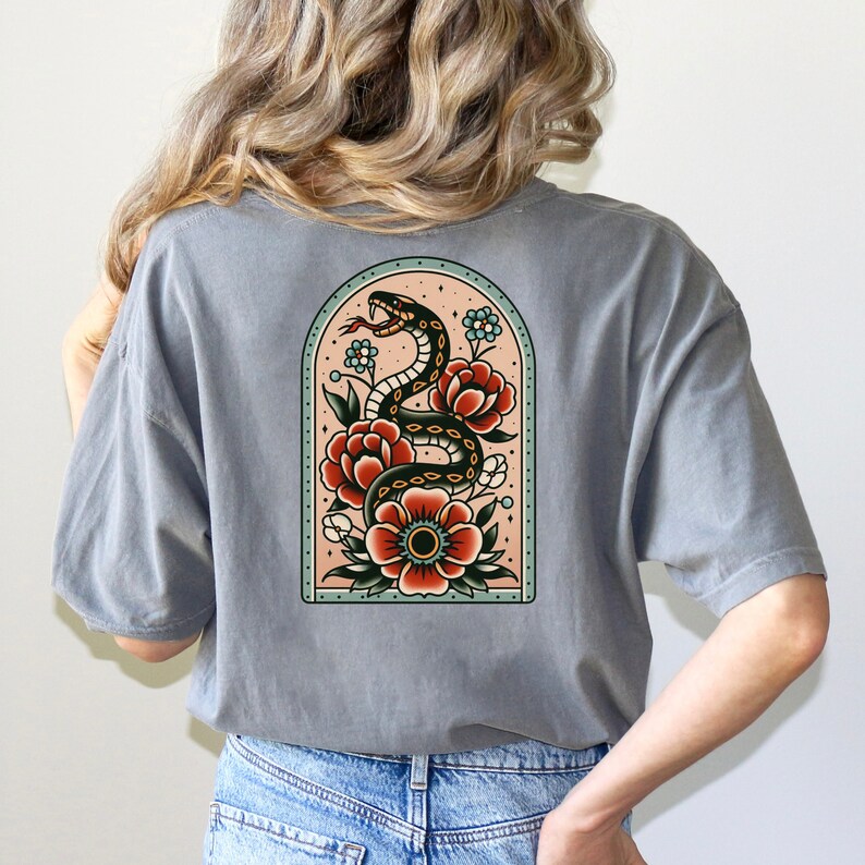 K&ouml;nnte beinhalten: Ein graues T-Shirt mit einer Vintage-Illustration einer schwarzen Schlange, die sich um rote und wei&szlig;e Blumen in einem t&uuml;rkisfarbenen Bogen windet.