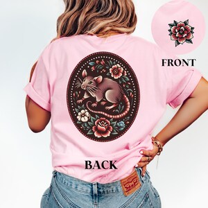May include: Pink t-shirt with a floral design featuring a rat and the word "BACK" printed on the back.