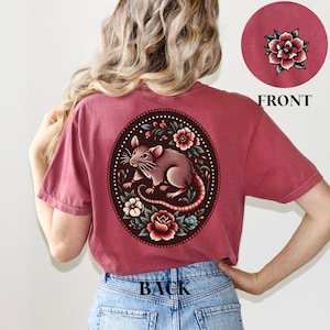 May include: A maroon t-shirt with a floral design featuring a rat on the back. The design is in a circle with a dark background and colorful flowers.