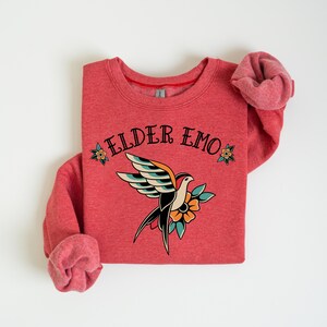May include: Red sweatshirt with a vintage-style bird and flower graphic and the text "ELDER EMO" in black.