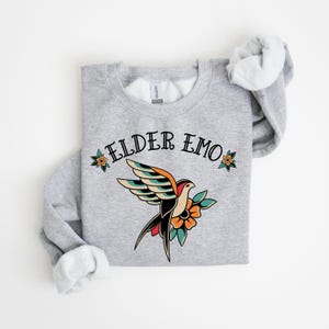 May include: Gray sweatshirt with the text "ELDER EMO" and a vintage-style tattoo of a bird with flowers.
