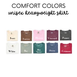 May include: A display of ten folded t-shirts in various colors, including ivory, white, espresso, bay, blossom, blue spruce, vineyard, denim, pepper, and crimson. The shirts are labeled with their color names.