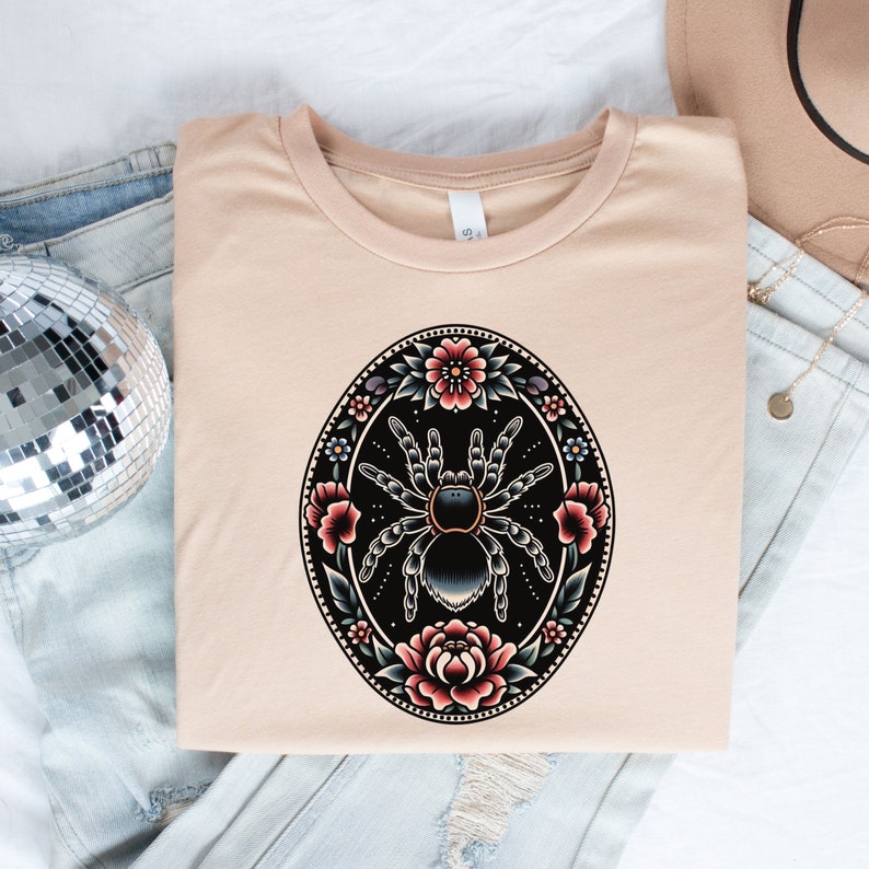 May include: A beige t-shirt with a black and gray tarantula spider surrounded by colorful flowers in a circular design.