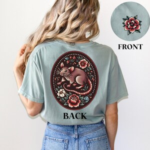 May include: A light blue t-shirt with a floral design featuring a rat and the word "BACK" printed on the back.