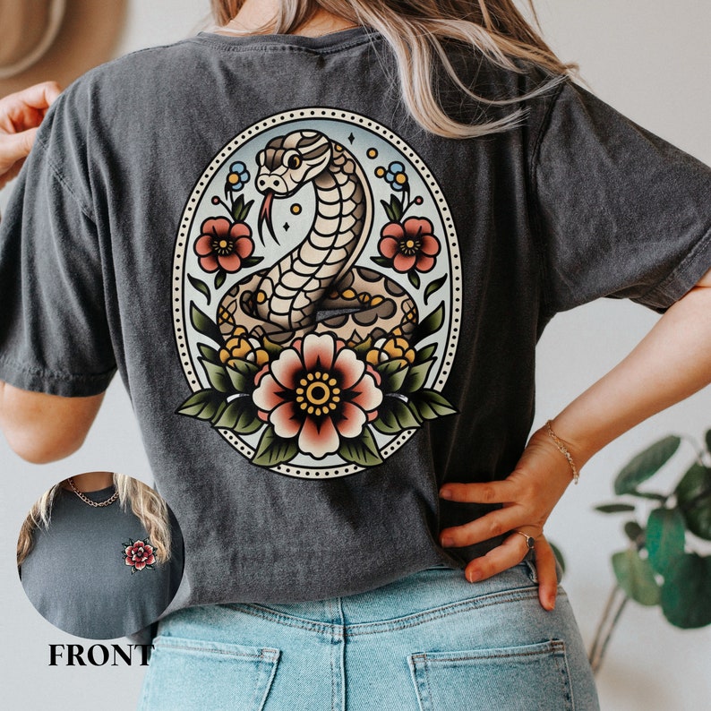 May include: A dark gray t-shirt with a vintage-style illustration of a snake coiled around flowers. The snake is brown and yellow, and the flowers are red, pink, and green. The illustration is surrounded by a circle with a dotted border.