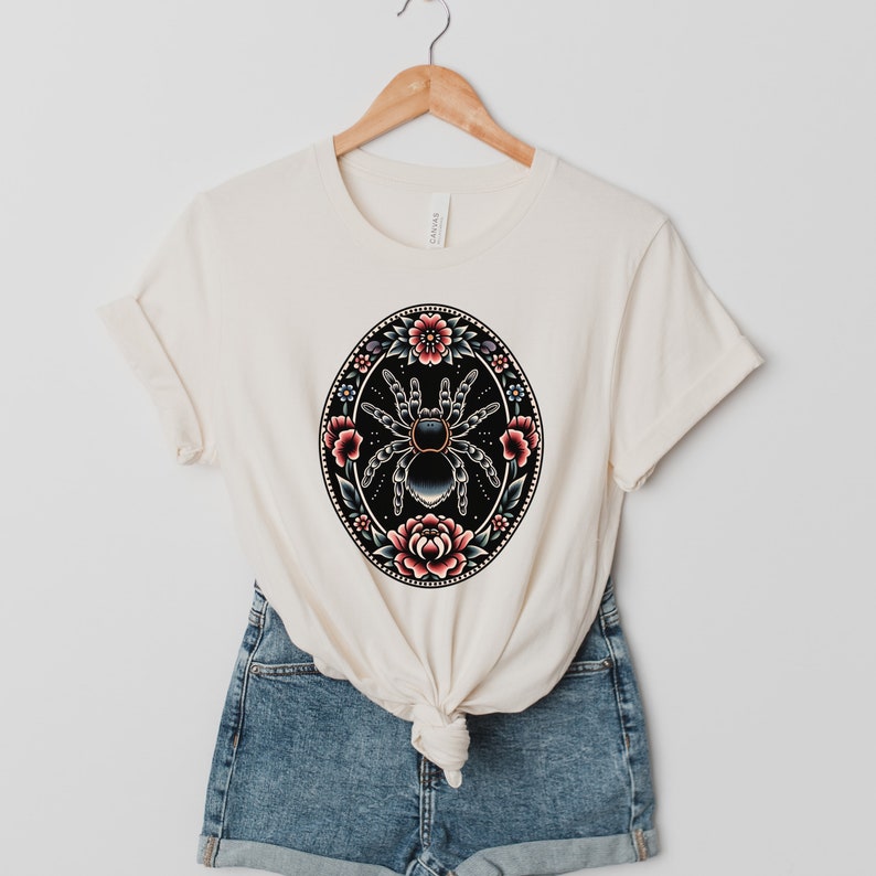 May include: A white t-shirt with a black and blue spider surrounded by pink and red flowers in a circular design.