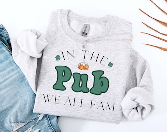 May include: A gray sweatshirt with the text "In the Pub We All Fam" in black lettering. The word "Pub" is in green with a retro font and two beer mugs are above it.