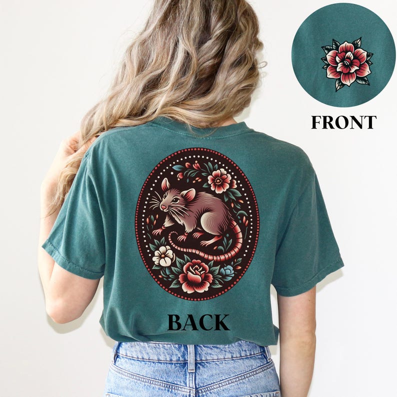 May include: Teal blue t-shirt with a floral design featuring a rat on the back. The design is in a circle with a white outline. The text "BACK" is printed below the design.