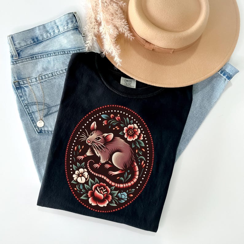 K&ouml;nnte beinhalten: Schwarzes T-Shirt mit einem floralen Design, in dessen Mitte sich eine Ratte befindet. Die Ratte ist braun und wei&szlig; mit einem langen Schwanz. Die Blumen sind rot, rosa und blau.