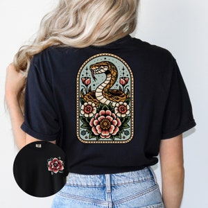 May include: Black t-shirt with a vintage-style illustration of a snake coiled around flowers in a frame. The design is on the back of the shirt.