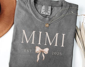 May include: A gray t-shirt with the word "MIMI" printed in white with a pink bow underneath. The text "EST 2025" is printed below the bow.