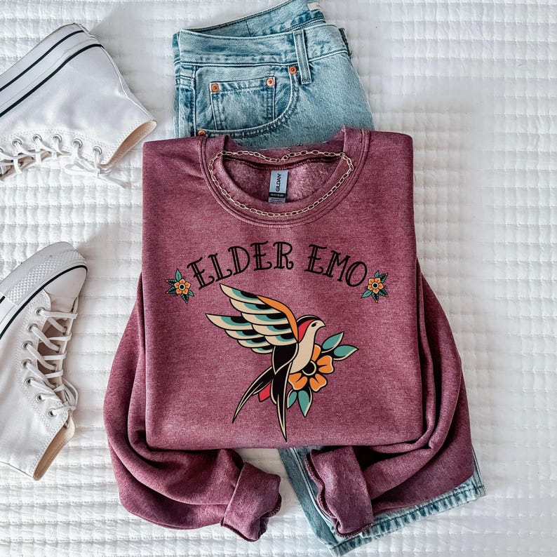 May include: A maroon sweatshirt with the text "ELDER EMO" and a vintage-style tattoo of a bird with flowers.