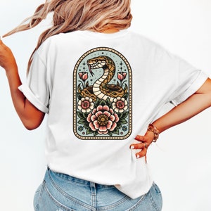 May include: White t-shirt with a vintage-style illustration of a snake coiled around flowers. The illustration is framed in a gold oval with a blue background.
