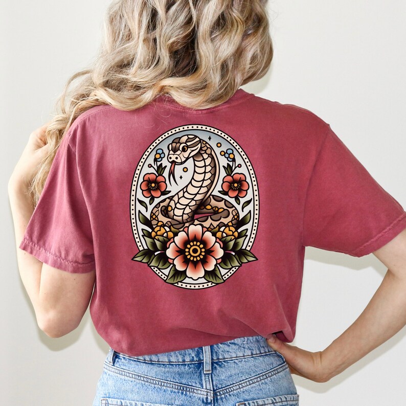 May include: A maroon t-shirt with a vintage-style illustration of a snake coiled around flowers. The snake is brown and white, and the flowers are red, yellow, and green.