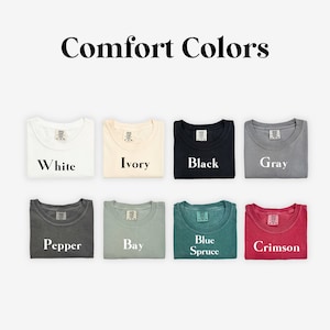 K&ouml;nnte beinhalten: Eine Sammlung von zehn gefalteten T-Shirts in verschiedenen Farben, darunter Wei&szlig;, Elfenbein, Schwarz, Grau, Pfeffer, Bucht, Blauer Fichte und Scharlachrot. Die Shirts sind in zwei Reihen zu f&uuml;nf angeordnet, wobei die Farben unter jedem Shirt beschriftet sind.