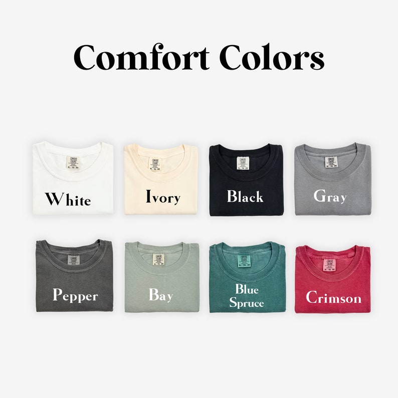 K&ouml;nnte beinhalten: Eine Sammlung von zehn gefalteten T-Shirts in verschiedenen Farben, darunter Wei&szlig;, Elfenbein, Schwarz, Grau, Pfeffer, Bucht, Blauer Fichte und Scharlachrot. Die Shirts sind in zwei Reihen zu f&uuml;nf angeordnet, wobei die Farben unter jedem Shirt beschriftet sind.