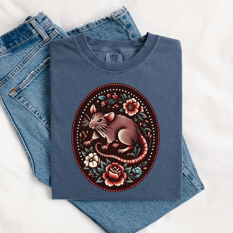 K&ouml;nnte beinhalten: Ein marineblaues T-Shirt mit einem floralen Design, das eine braune Ratte zeigt. Die Ratte ist von roten, wei&szlig;en und rosa Blumen umgeben.