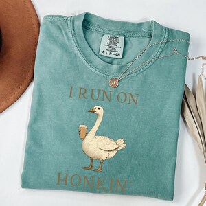May include: A teal blue t-shirt with a brown goose graphic and the text "I run on honkin'" printed on the front.