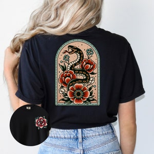 K&ouml;nnte beinhalten: Schwarzes T-Shirt mit einem Tattoo-Design im Vintage-Stil, das eine Schlange zeigt, die sich um Blumen in einem Bogenrahmen windet.