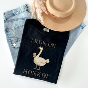 May include: Black t-shirt with a white goose holding a cup of coffee and the text "I run on honkin'" printed in brown.