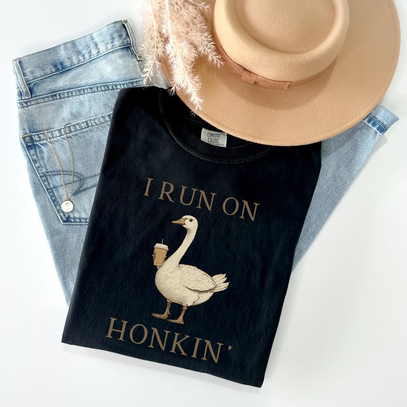 May include: Black t-shirt with a white goose holding a cup of coffee and the text "I run on honkin'" printed in brown.