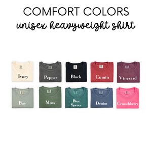 K&ouml;nnte beinhalten: Eine Auswahl von zehn gefalteten T-Shirts in verschiedenen Farben, darunter Elfenbein, Pfeffer, Schwarz, Kreuzk&uuml;mmel, Weinrebe, Bucht, Moos, Blautanne, Denim und Cranberry. Die Shirts sind mit ihren Farbnamen beschriftet.