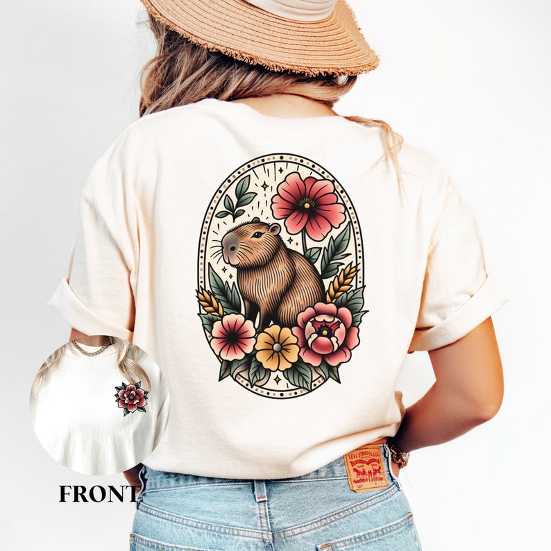 K&ouml;nnte beinhalten: Ein wei&szlig;es T-Shirt mit einem floralen Design, das ein Capybara, Blumen und Bl&auml;tter zeigt. Das Design ist im Vintage-Stil gehalten und wird von einem Kreis mit gepunktetem Rand eingerahmt.