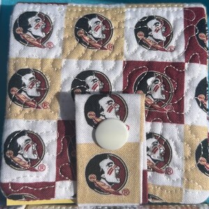 May include: A white and maroon quilted fabric wallet with a repeating pattern of a Seminole State University logo. The wallet has a snap closure and a white button.