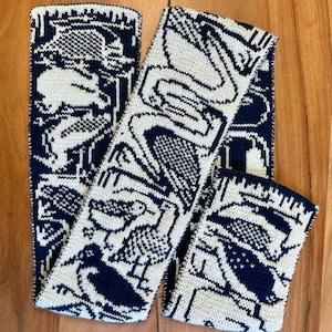 Puede incluir: Bufanda de punto y calentadores de mu&ntilde;eca a juego en crema y azul marino. El patr&oacute;n presenta aves estilizadas y formas geom&eacute;tricas. La bufanda est&aacute; doblada y los calentadores de mu&ntilde;eca est&aacute;n sobre una superficie de madera.