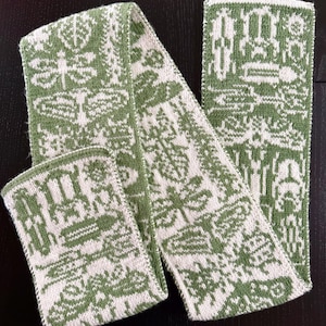 May include: A green and white knitted scarf and matching wrist warmer set. The scarf and wrist warmer feature a repeating pattern of stylized botanical and insect motifs. The scarf is folded and laid out on a dark surface.