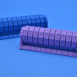 May include: Two number counters in the image. One is blue, the other is purple. Each counter has rotating number wheels from 0 to 9. The purple counter also has the letters "CF". The background is a solid blue.
