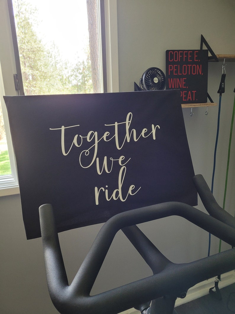 May include: A black exercise bike with a motivational sign that reads "Together we ride" in white lettering.